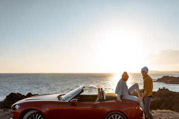 Couple enjoying beautiful views on the ocean, standing together near the car on the rocky coast, wide view from the side with copy space