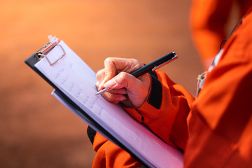 Wall Mural - Safety officer/Supervisor is writing note on the checklist paper during perform audit and inspection in oil field operation. Close-up action and selective focus photo.