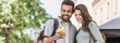 Beautiful happy young couple using smartphone outdoors panoramic banner. Joyful smiling woman and man looking at mobile phone in a city. Love, technology, communication, summer travel concept