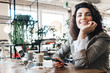 © Alex from the Rock - Portrait of pretty young woman in coffee house. Wearing smart casual suit and sitting with laptop in public cafe. Holds mobile phone in hand and drinking coffee