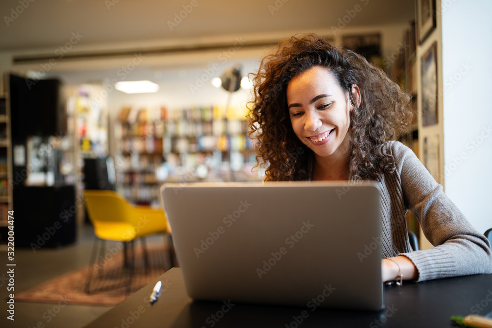 Young beautiful student girl working, learning in college library - obrazy, fototapety, plakaty 
