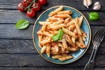 Poster - Penne pasta in tomato sauce and cheese decorated with basil on a wooden background, top view