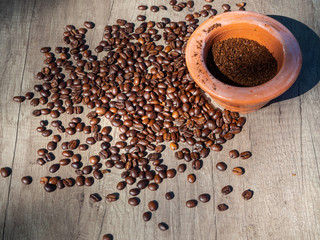  Black coffee ground in a clay mortar and in grains on the surface of a wooden table in sunny rays.