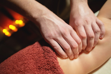 Wall Mural - Men's premium luxury hip massage anti-cellulite wellness center. Close-up of a male masseur doing leg massage to a female client in an office with dark light on a background of burning candles