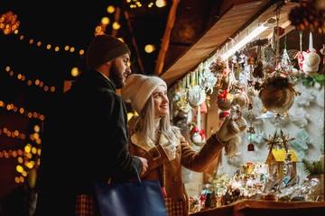 Happy smiling couple shopping at Christmas street market, choosing gifts. Winter holidays, vacation, travel, purchase conception