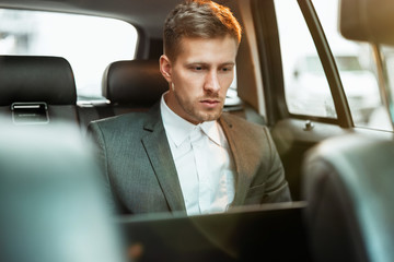 Wall Mural - young businessman works in his laptop while sitting in his car on his way to office, multitasking concept