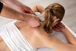 High angle view of therapist holding electro stimulation electrodes near neck of woman on massage couch
