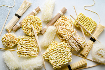 Variety of uncooked asian noodles on light background, closeup view