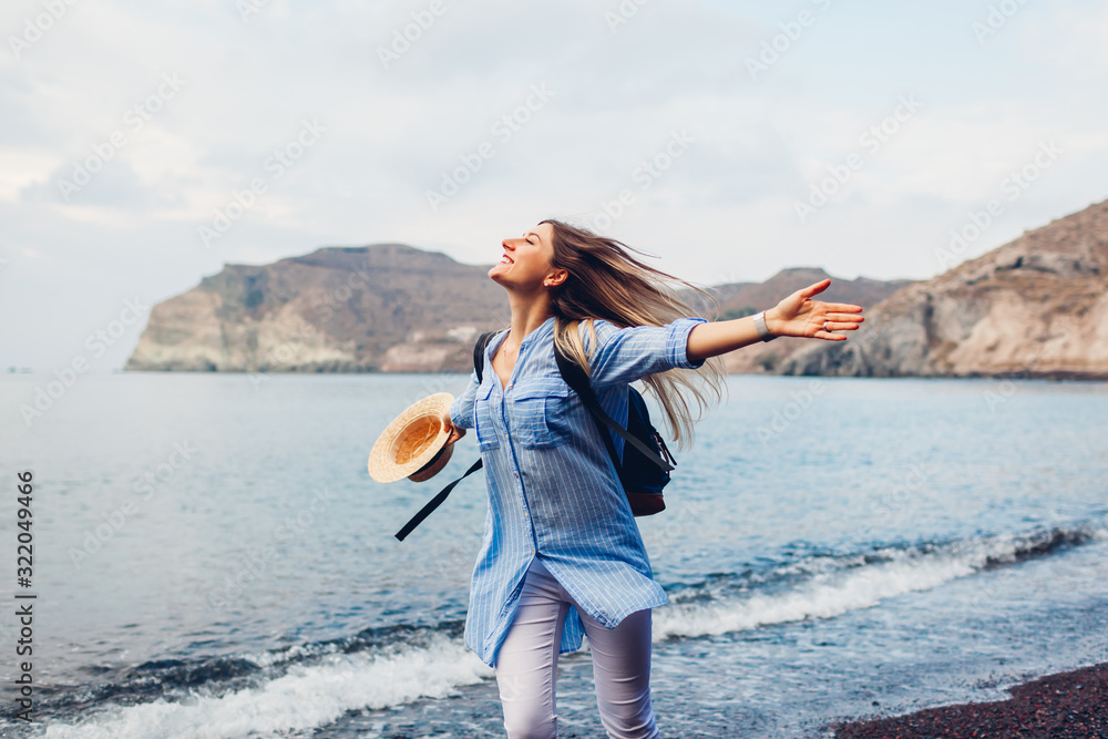 Traveler woman running along shore of Red beach on Santorini island, Greece. Traveling and vacation concept - obrazy, fototapety, plakaty 