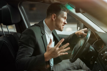 Wall Mural - young angry businessman sitts in his car looks anxious after hard day at workplace, stressfull working conditions concept