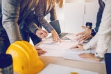 Fototapeta  - Group of dedicated hardworking highly motivates architects looking and pointing at blueprints on desk inside of building they want to renew.