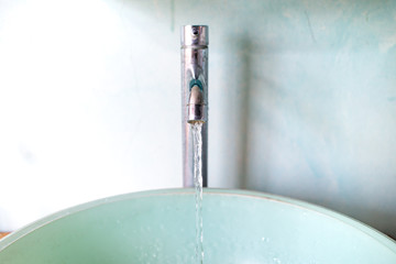 Water flowing from faucet to green washbasin, Bathroom concept