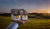 Fototapeta  - Concept of buying or building new home. Male hand showing, offering a new dream house at the empty field with copy space