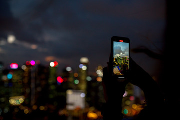 A girl takes pictures of the night city from a skyscraper in Singapore and Kuala Lumpur on her phone