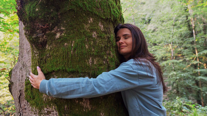 A woman in the forest embraces a large tree.