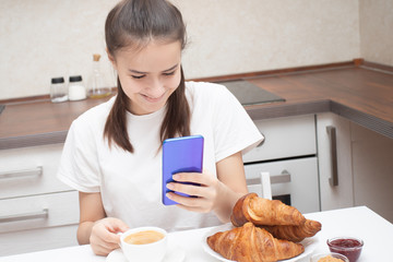 A young girl looks at a smartphone, communicates on social networks at breakfast