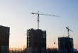 © MaxSafaniuk - Silhouettes of tower cranes constructing a new residential building at a construction site against sunset background. Renovation program, development, concept of the buildings industry.