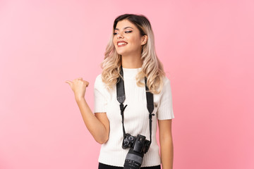 Wall Mural - Teenager girl over isolated pink background with a professional camera and pointing to the side