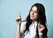 Young smiling sexy brunette woman in white medical uniform is holding cosmetology tools over blue background