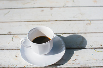 Cup of coffee on white wooden background with warm sunlight in the morning.