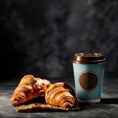 Wall Mural - Fresh hot coffee in paper cup and tasty croissants on dark mood background. 