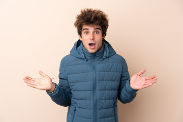 Man wearing winter jacket over isolated background with shocked facial expression