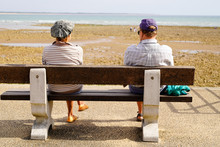 Senior Retired Elderly Couple Sitting On A Bench Looking Ocean Atlantic Seaside In Low Tide