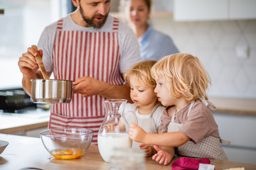 Young family with two small children indoors in kitchen, cooking.