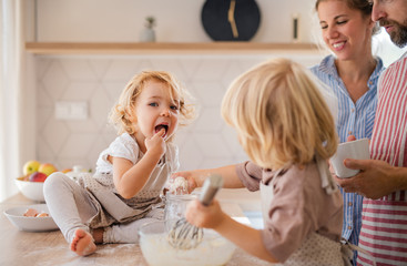 young family with two small children indoors in kitchen, cooking.