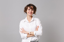 Smiling Attractive Young Business Woman In White Shirt Posing Isolated On Grey Wall Background Studio Portrait. Achievement Career Wealth Business Concept. Mock Up Copy Space. Holding Hands Crossed.