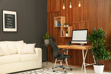 Poster - Comfortable workplace with computer near wooden wall in stylish room interior. Home office design