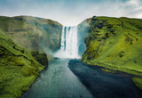 View from flying drone. Dramatic midnight sun view of Skogafoss Waterfall. Stunning summer landscape of Skoga river, Iceland, Europe. Green filter toned.