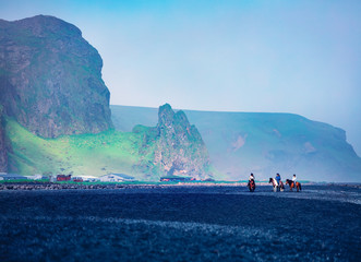 horseback riding on the famous black sand beach in vik village. amazing summer scene of icelan, euro