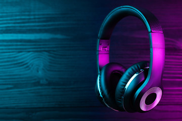 Black headphone on dark wooden background. Stylish wireless headset in neon light.