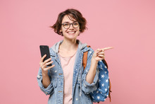 Smiling Girl Student In Denim Clothes Glasses Backpack Isolated On Pastel Pink Background. Education In High School University College Concept Using Mobile Phone Typing Sms Message Point Finger Aside.