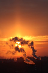 Wall Mural - red sun at sunset or dawn at dusk low above the horizon shrouded in smoke from the chimneys of the p
