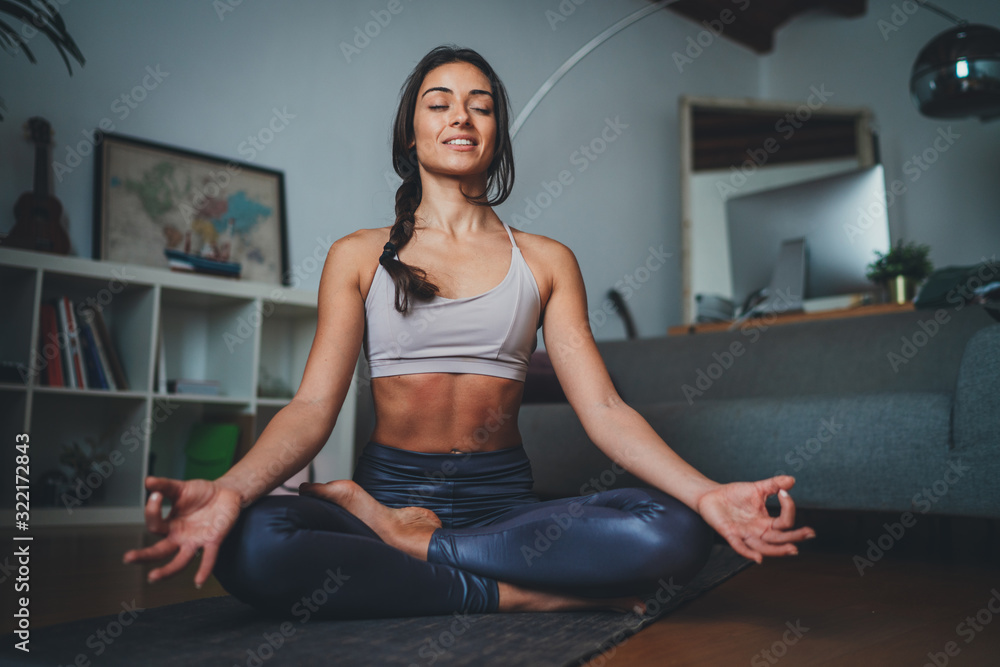 Young beautiful woman meditating at modern home interior sitting on yoga mat and smiling relaxed with closed eyes, Mindfulness meditation concept, Healthy Lifestyle - obrazy, fototapety, plakaty 