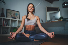 Young Beautiful Woman Meditating At Modern Home Interior Sitting On Yoga Mat And Smiling Relaxed With Closed Eyes, Mindfulness Meditation Concept, Healthy Lifestyle