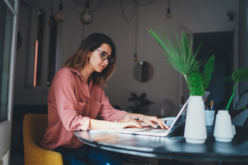 Wall Mural - Young female entrepreneur working remotely from a home office using modern laptop computer, woman copywriter working online 