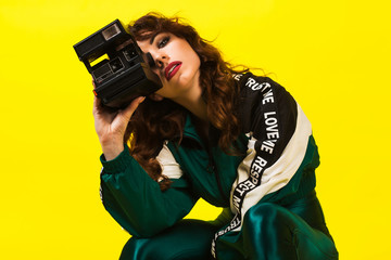 Cheerful gorgeous girl in clothes in the style of the 90s, with a vintage camera with quick shots, in the studio on a white background, emotions, fashion