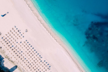 Poster - Top-down aerial view of a clean beach equipped with umbrellas and sunbeds on the turquoise sea. Greece.