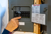 Canadian House Distribution Board, Circuit Breaker Panel With Interchangeable Circuit Breakers. Woman's Hand Pointing And Clicking On A Breaker.
