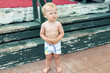 Cute funny upset caucasian 2 year old toddler boy standing abandoned alone at beach summer day. Offended scared child lost parents during vacation. Blond feared kid with suspicious facial expression