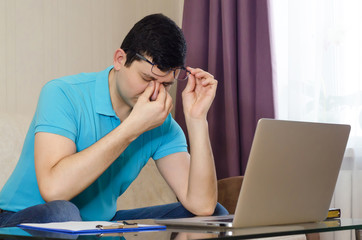 tired male businessman, worker, freelancer with headache and tension in the eyes from glasses over a computer. fatigue from work.