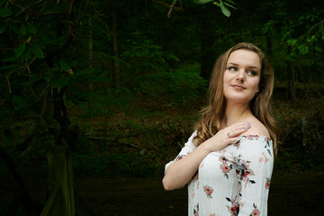 Wall Mural - Stunning young blonde woman poses in woods wearing floral off-the shoulder blouse and blue jeans - spring fashion