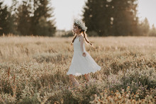 Happy Joyful Young Girl In A White Dress And With A Flower Wreath On Her Head In The Field In The Summer