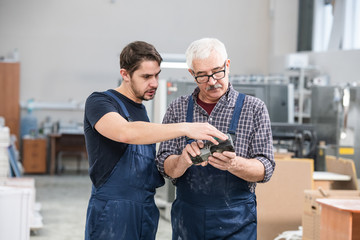 Wall Mural - Young specialist in overall showing senior coworker how to use controller at factory