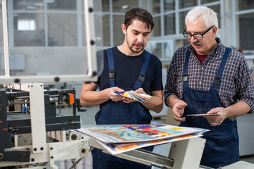 Busy printing plant workers standing at printed pages and choosing colors for next printing