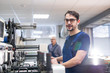 © pressmaster - Portrait of content young printing specialist in glasses standing at printing press