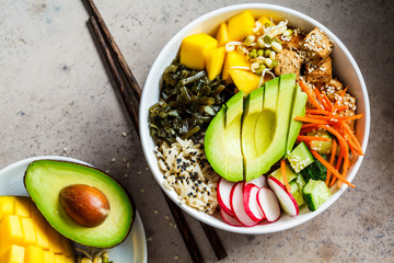 Wall Mural - Vegan poke bowl with avocado, tofu, rice, seaweed, carrots and mango, top view. Vegan food concept.